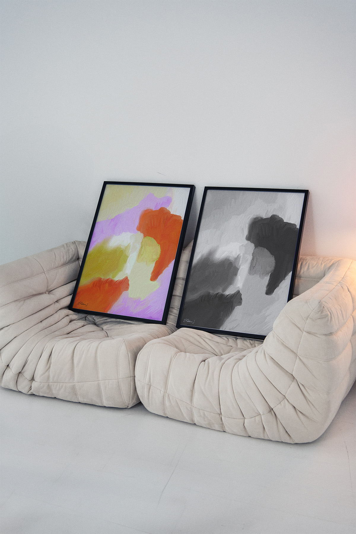 Contemporary art wall with vibrant abstract pieces in orange, pink, yellow, gray, and black, displayed in a cozy, Scandinavian-inspired room.